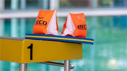 Zwei Schwimmflügel und ein Schwimmbrett liegen auf einem Startblock in der Schwimmhalle des Moskaubads.