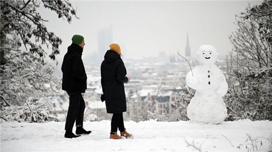 Zwei Spaziergänger wandern am Fockeberg (Leipzig) an einem Schneemann vorbei.