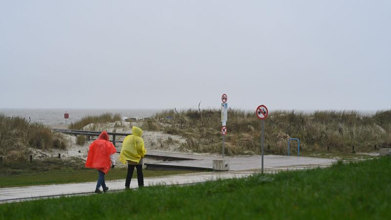 Zwei Tagesgäste laufen bei nassem Wetter in Regenjacken an der Starndpromenade entlang.