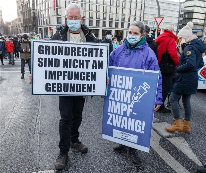 Zwei Teilnehmer einer Demonstration gegen die Corona-Maßnahmen zeigen ihre Plakate. Seit dieser Woche muss in Hamburg bei Demonstrationen Mund-Nasen-Schutz getragen werden. Foto: Markus Scholz/dpa