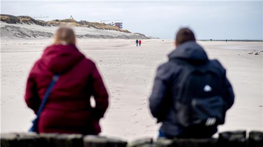 Zwei Touristen sitzen auf den Holzpfählen einer Buhne am Strand von Wangerooge – die ruhige Insel ist gerade bei Familien und Menschen mit Hund sehr beliebt.