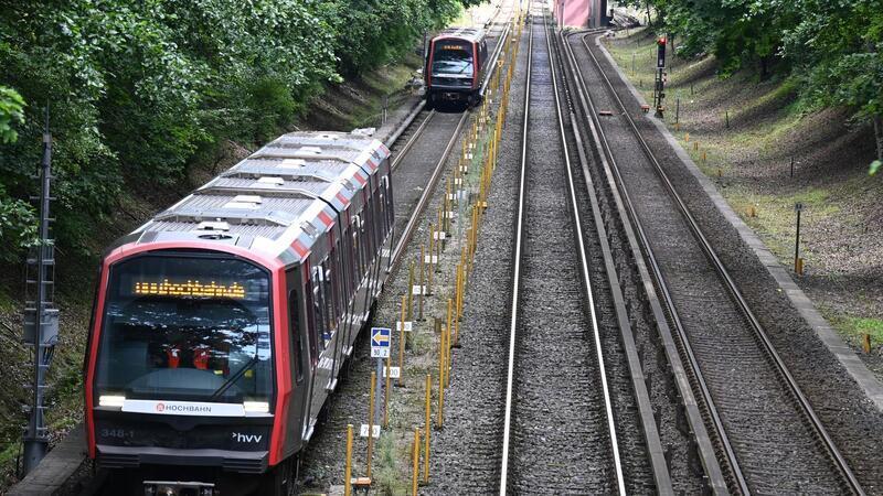 Zwei U-Bahnen der Hochbahn fahren in dichtem Abstand über die Gleise.