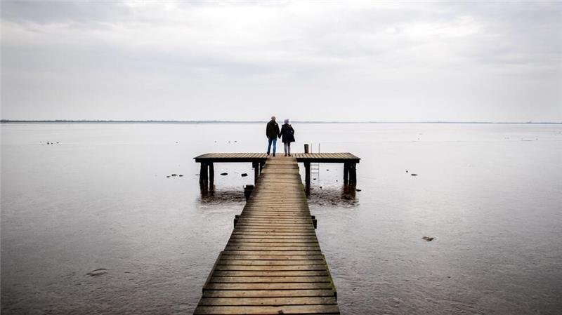 Zweisamkeit: Ein Paar geht bei trübem Wetter über einen Holzsteg am Jadebusen im niedersächsischen Dangast.