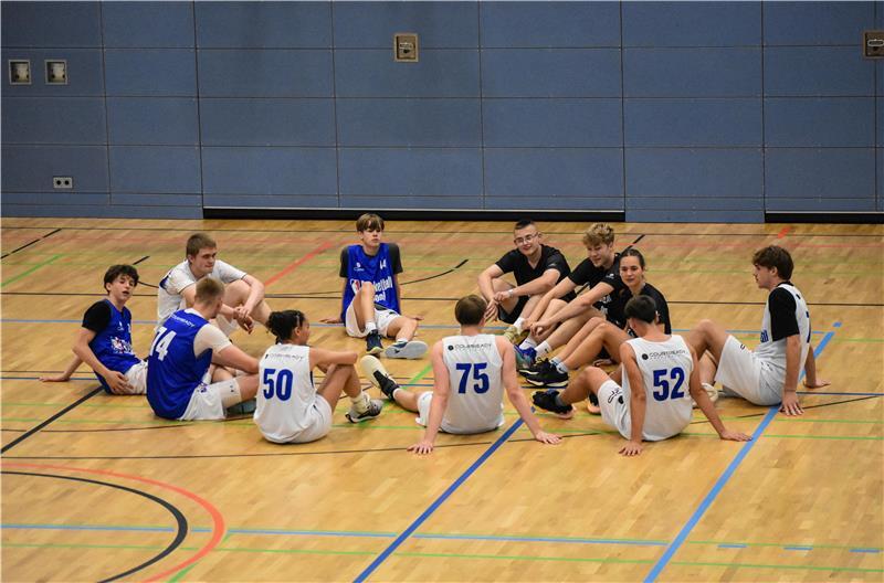 NBA-Camp in Stade: Junge Basketballer lernen von den Profis Spieler und Trainer sitzen im Kreis zusammen auf dem Parkett und tauschen sich aus.