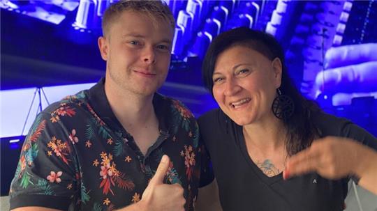  Alexander Krischer und Kristin Probst stehen vor einem TV-Still mit Nahaufnahme eines DJ-Pultes